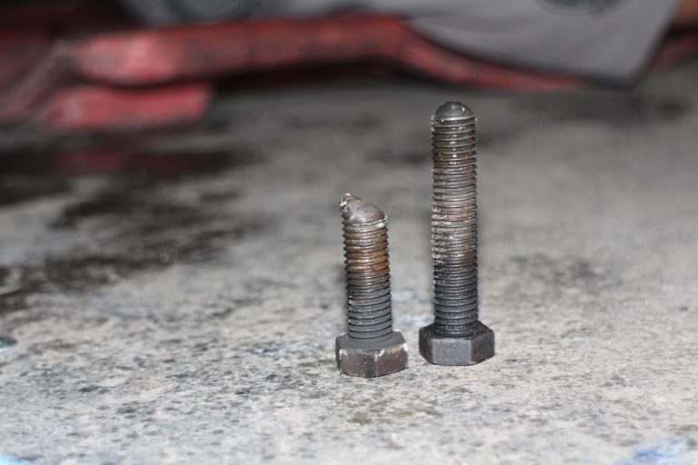 He removed the bolt that adjusts the cam on the end of the driver-side torsion bar and found that it was sheared half its length. He also removed the bolt on the passenger side torsion bar cam for comparison.